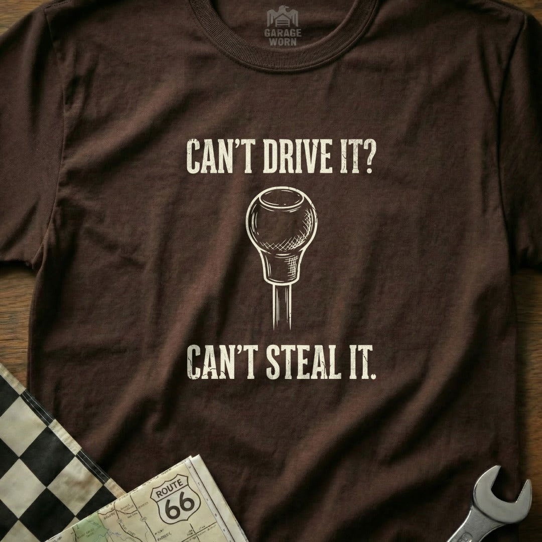 Brown t-shirt with text "CAN'T DRIVE IT? CAN'T STEAL IT." and a gear shift.