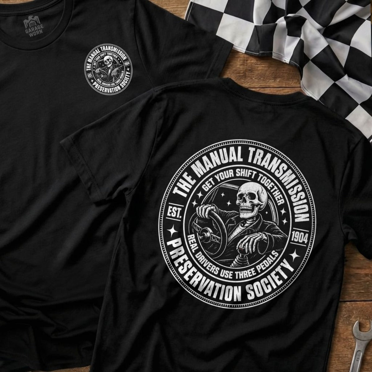 Black t-shirt with a circular graphic of a skeleton driving and "The Manual Transmission Preservation Society" text.