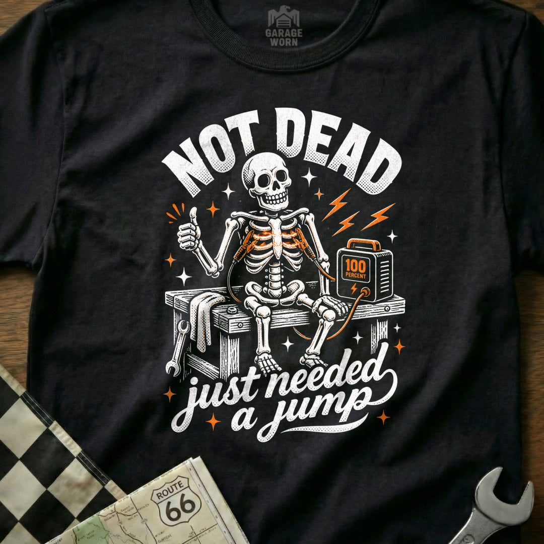 Black t-shirt with skeleton saying "Not Dead, Just Needed a Jump" and jump starter.