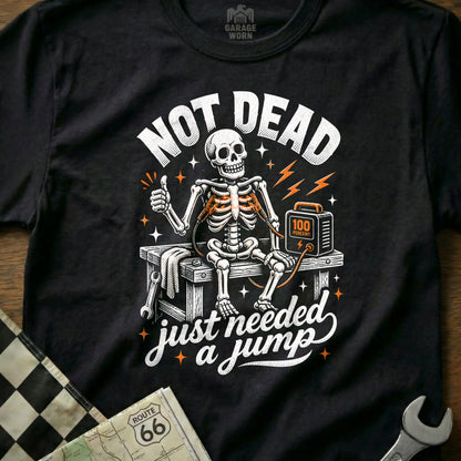 Black t-shirt with skeleton saying "Not Dead, Just Needed a Jump" and jump starter.
