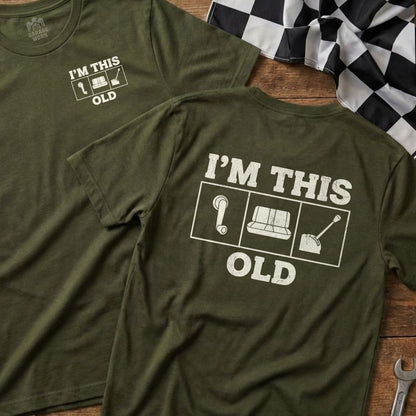 Olive green t-shirt with white text and icons: "I'M THIS OLD" with question mark, couch, and shovel.
