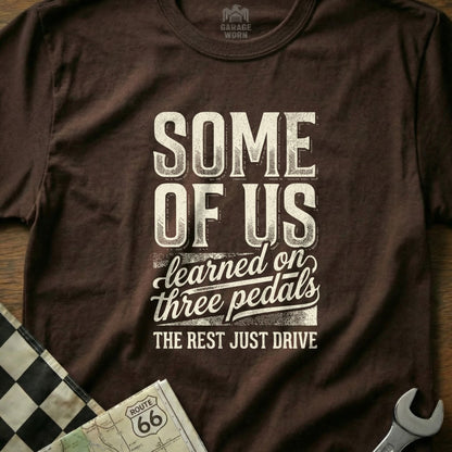 Brown t-shirt with "SOME OF US learned on three pedals, THE REST JUST DRIVE" text.