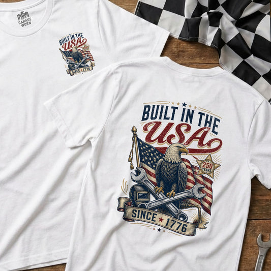 White t-shirt with "Built in the USA" graphic featuring an eagle, American flag, and tools.