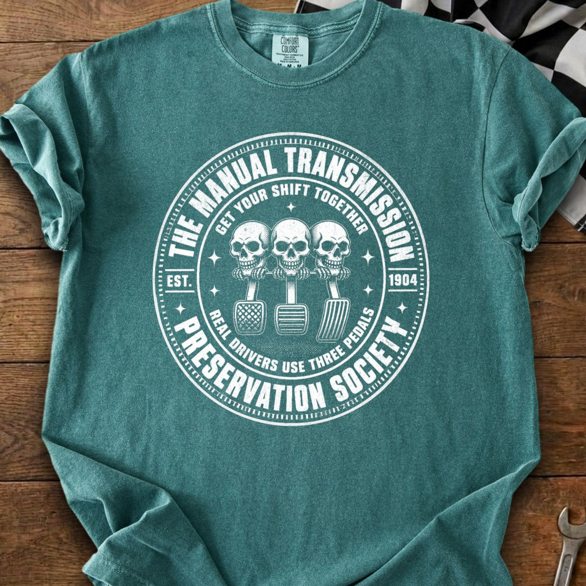Teal t-shirt with white graphic of three skulls with three pedals: "The Manual Transmission Preservation Society".