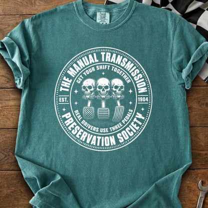 Teal t-shirt with white graphic of three skulls with three pedals: "The Manual Transmission Preservation Society".