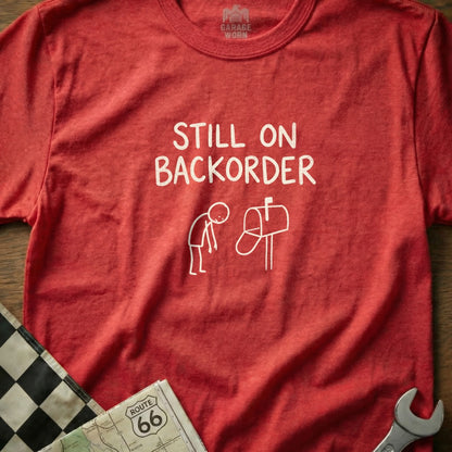 Red t-shirt with "Still on Backorder" text and stick figure at mailbox.