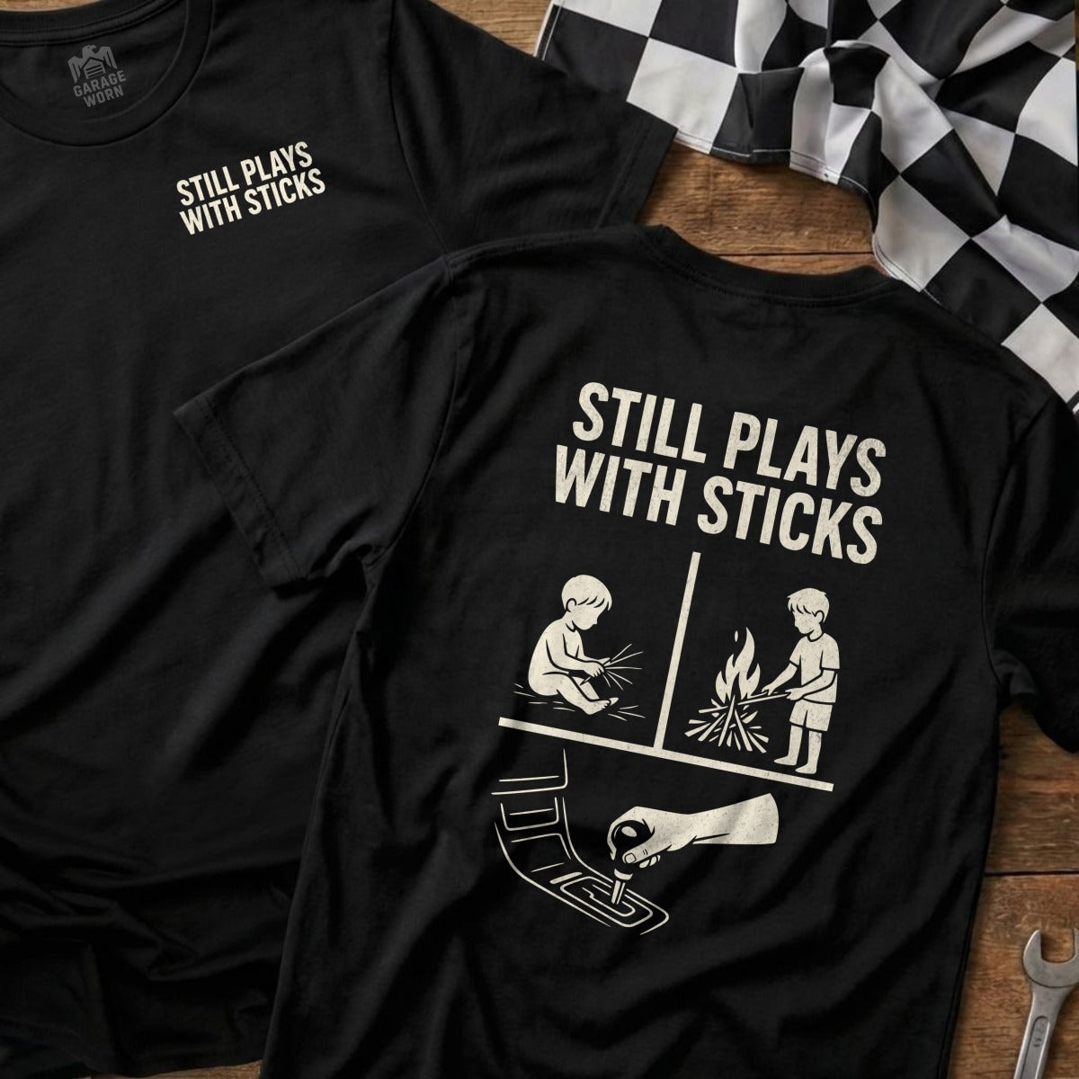 Black t-shirt with "STILL PLAYS WITH STICKS" and graphic of a controller and campfire.