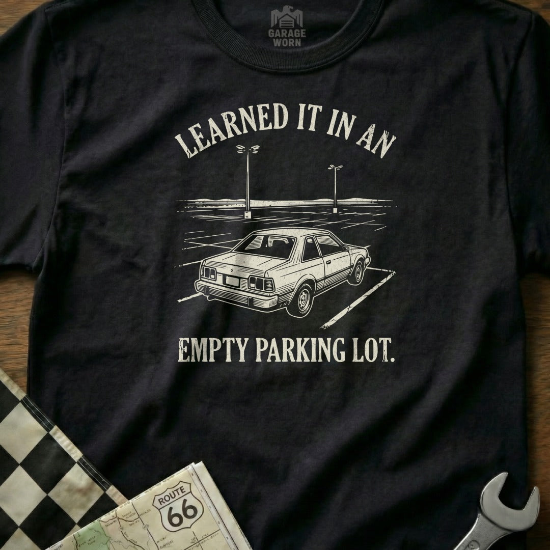 Black t-shirt with white text and graphic of a car in an empty parking lot.