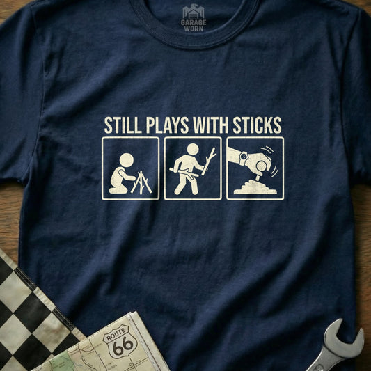 Navy t-shirt with white graphic: figures playing with sticks, with text "STILL PLAYS WITH STICKS".