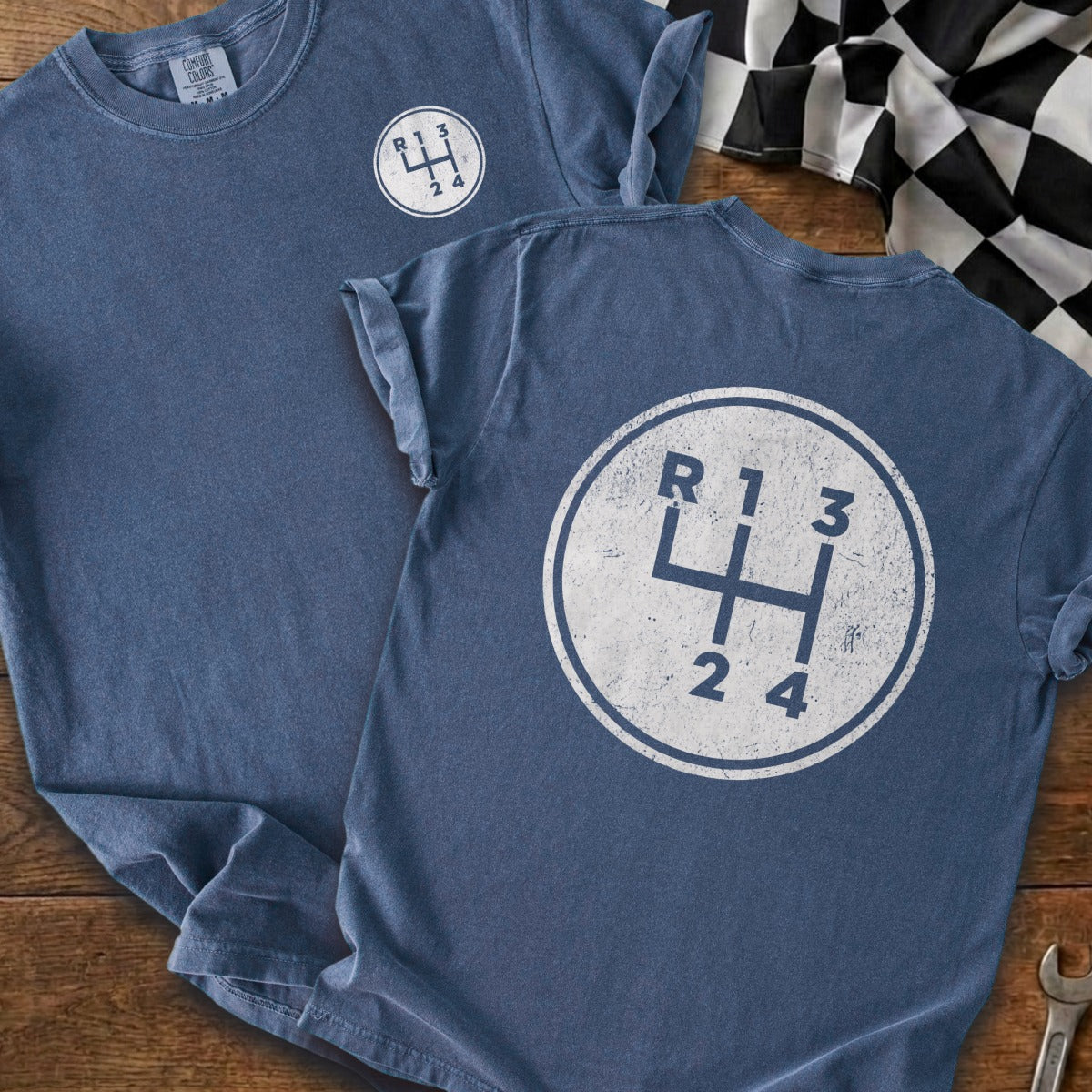 Blue t-shirt with a distressed graphic of a manual gear shift pattern and racing flag.