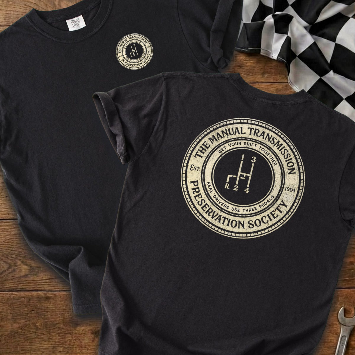Black t-shirt with circular logo featuring a manual transmission shifter and text.