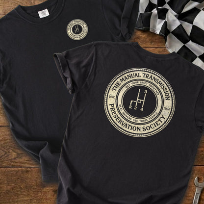 Black t-shirt with circular logo featuring a manual transmission shifter and text.