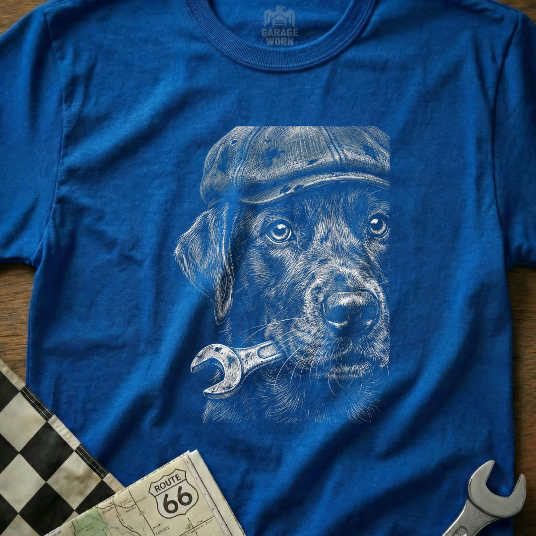 Sketch of a dog in a cap holding a wrench in its mouth on a blue t-shirt.