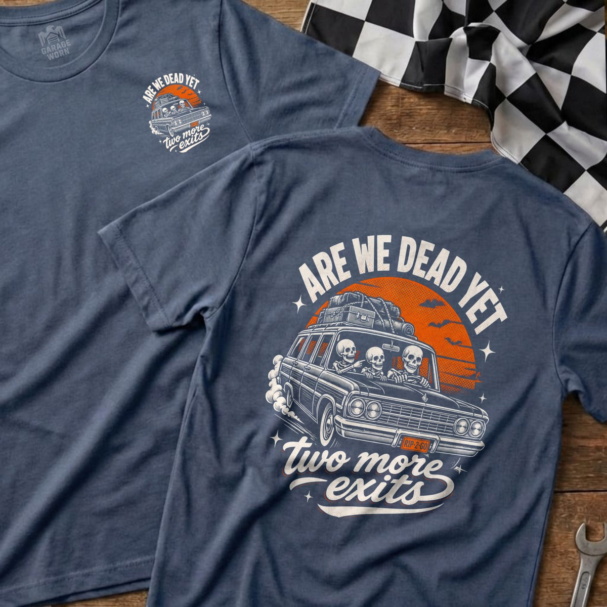T-shirt with graphic of skeletons driving a car, text "ARE WE DEAD YET two more exits".