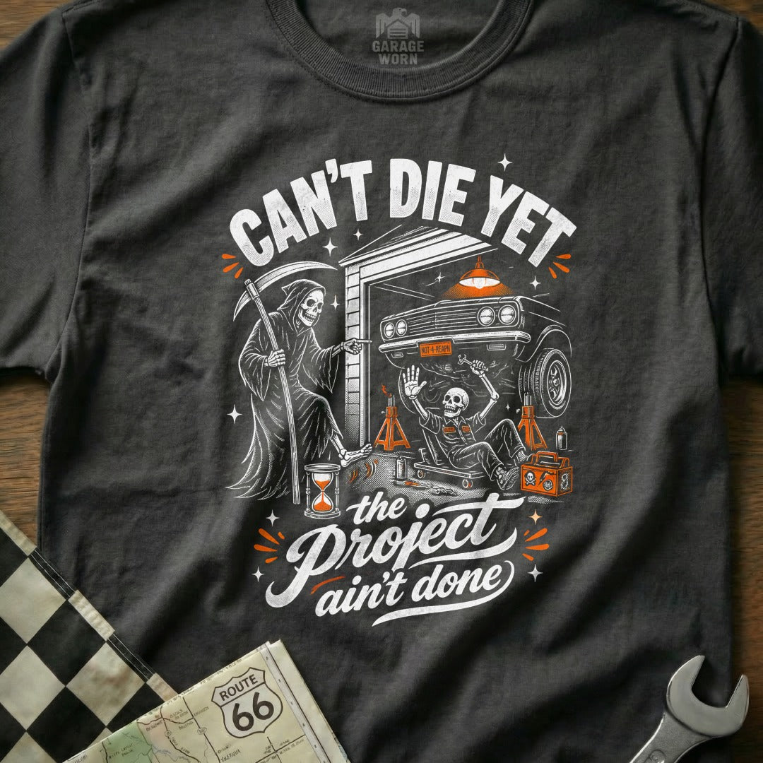 T-shirt graphic: Grim Reaper points at skeleton working on car, text "Can't Die Yet".