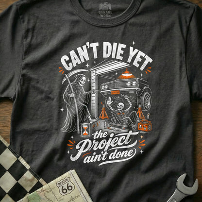T-shirt graphic: Grim Reaper points at skeleton working on car, text "Can't Die Yet".