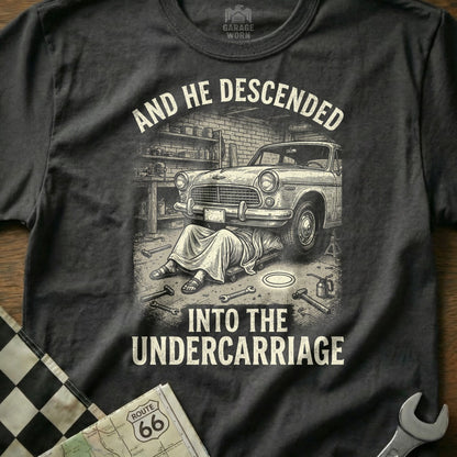 T-shirt design with man working under classic car, text reads "AND HE DESCENDED INTO THE UNDERCARRIAGE".