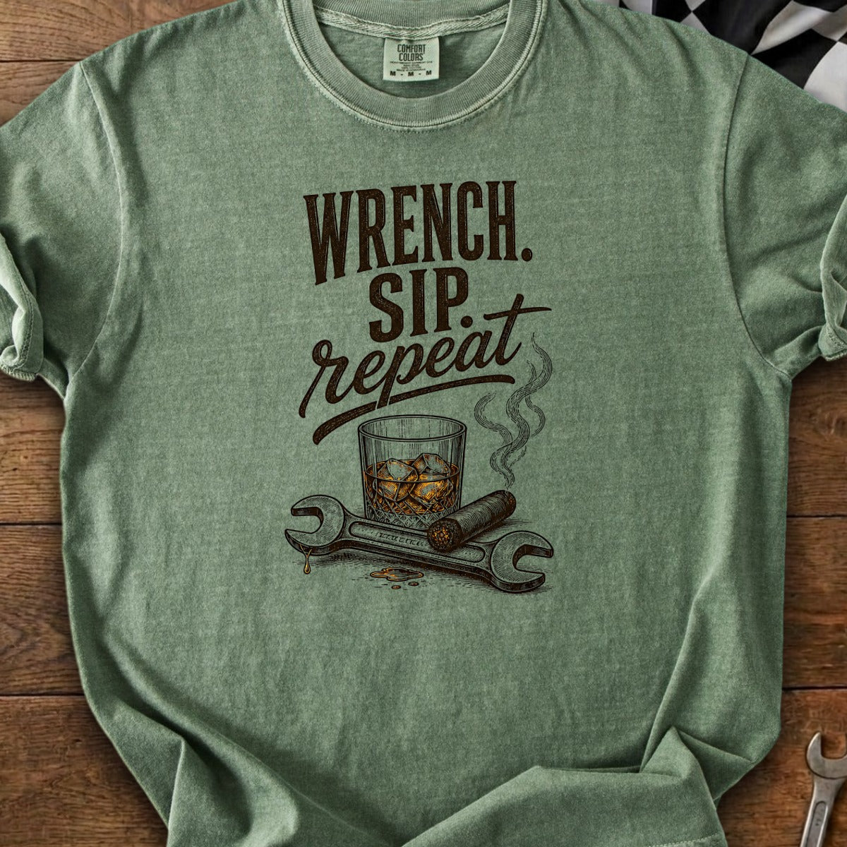 Green t-shirt graphic with text "Wrench. Sip. Repeat.," whiskey glass, cigar, and wrenches.