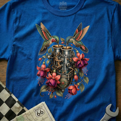 Two hummingbirds drink from a vintage carburetor surrounded by fuchsia flowers.