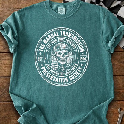 T-shirt features a circular graphic with a skeleton giving a thumbs-up, reading "The Manual Transmission Preservation Society."