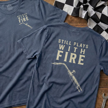 Navy t-shirt with "Still Plays With Fire" and a blowtorch graphic.