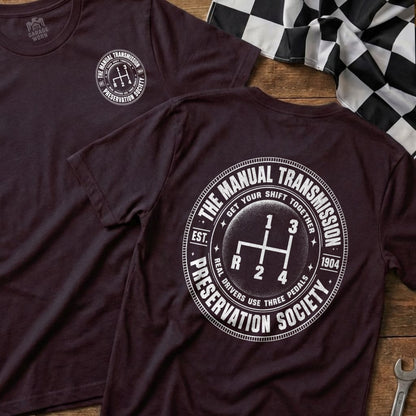 Dark t-shirt features a white graphic of a manual transmission shifter and "The Manual Transmission Preservation Society".