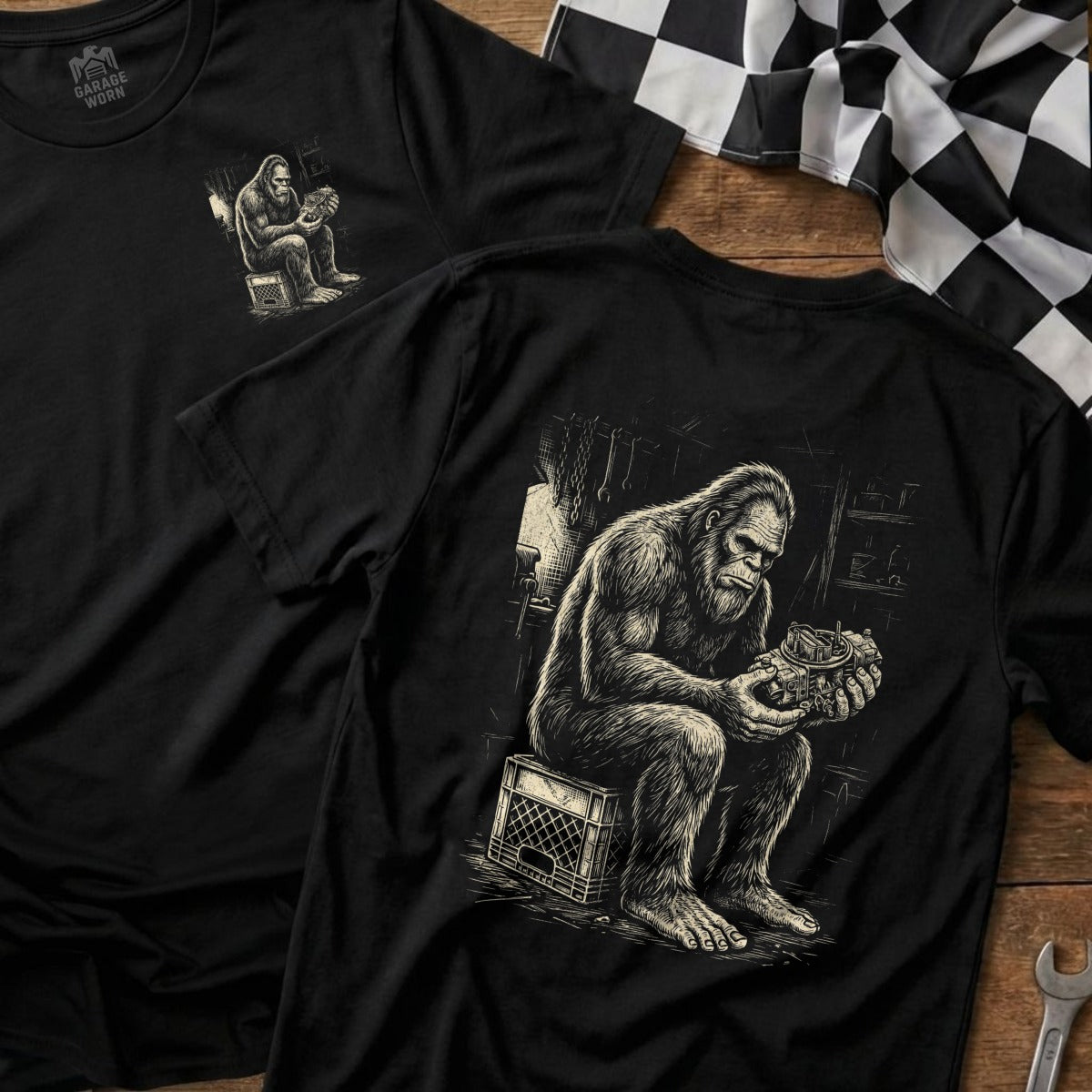 Black t-shirt with Bigfoot illustration of him working on an engine part.