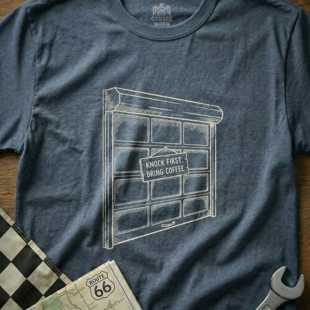 T-shirt with a drawing of a garage door with a "Knock First, Bring Coffee" sign.