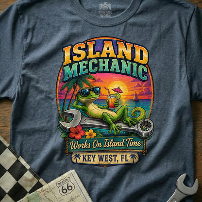 Green lizard with sunglasses rests on a wrench, drinking a cocktail over a tropical sunset scene, reading "Island Mechanic".